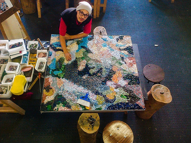 An aerial view of a maker working on a large abstract mosaic tabletop piece